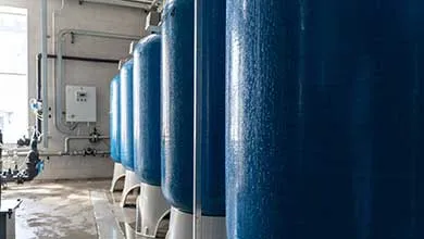 Row of large, blue, condensation-covered industrial water filtration tanks on a wet concrete floor.
