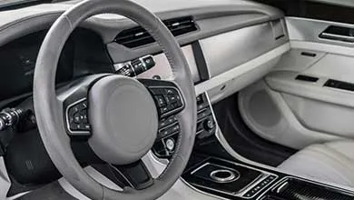 Close-up of a modern car's interior: gray leather steering wheel and a sleek, silver, and gray dashboard.