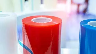 Close-up of three large upright rolls of plastic film in white, red, and blue.