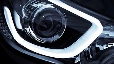 Close-up of a modern car headlight featuring a bright white LED strip curving around the main lens.