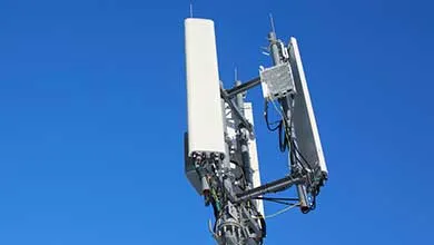 Close-up of a cell tower top with several white rectangular antennas against a bright blue sky.