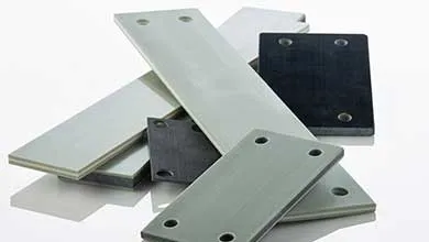 Stacked rectangular thermoset composite plates in gray and black with drilled mounting holes on a white background.