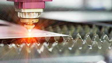 Industrial laser cutting head focused on a flat material surface, emitting a bright cutting beam and sparks.
