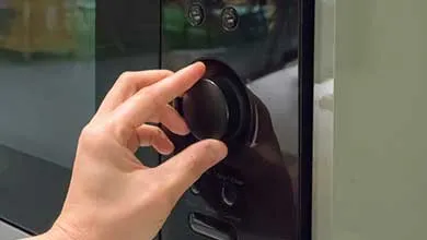 A hand turning a black rotary dial on a microwave oven control panel, with the glass door visible behind.