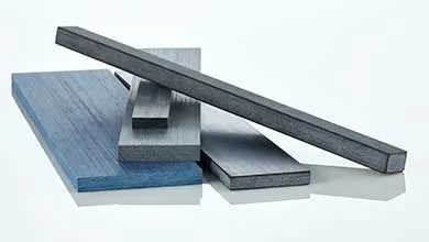 Rectangular blue and gray wood-grain planks are stacked on a white surface, with a long dark gray bar resting on top.